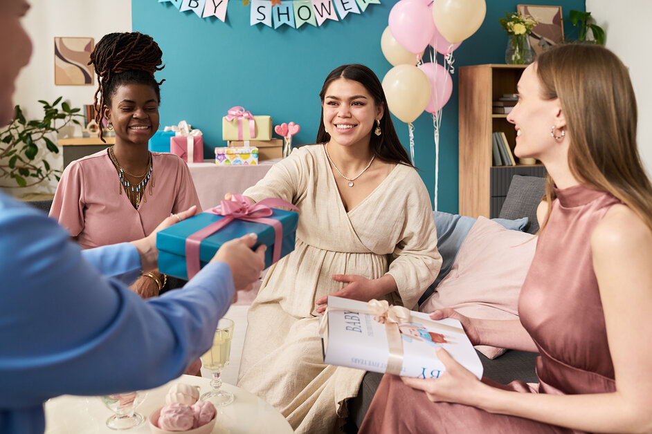 Guests laughing as a baby shower bingo winner unwraps a layered prize.